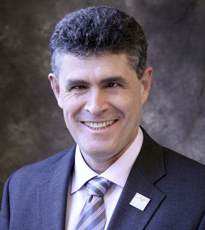 Joe Xavier wearing a navy suit jacket over white dress shirt with red and navy striped tie