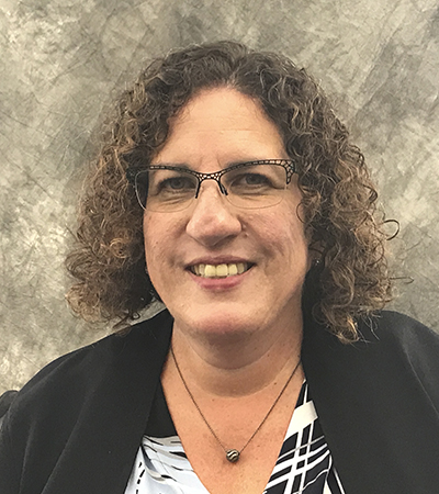 Woman with short curly hair wearing a blouse and suit jacket