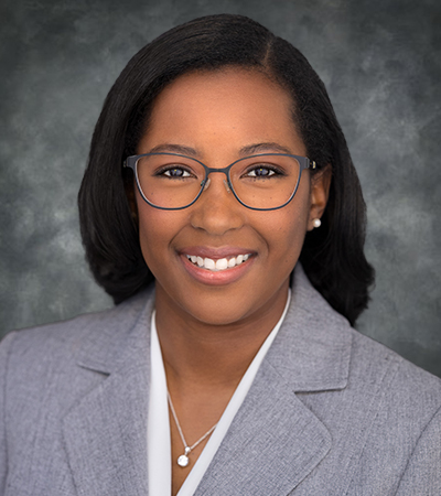 Woman with medium length, straight, black hair wearing glasses and a grey suit