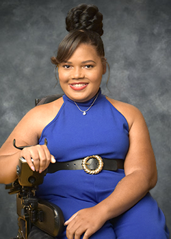 Candis Welch in a blue sleeveless jumper wearing a tiara against a smokey grey background