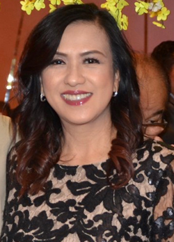 Woman with dark curled shoulder length hair wearing a white gown with black floral pattern