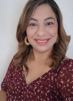 Woman with brown hair wearing gold hoop earrings and a red floral blouse