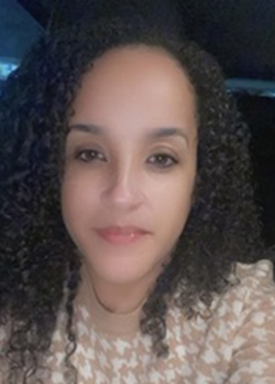 Woman with dark brown curly hair wearing a tan and white patterned blouse