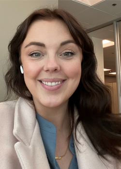 woman with long brown hair wearing a tan coat over blue blouse