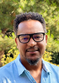 Man with short black hair and a peppered goatee wearing prescription glasses and a blue polo