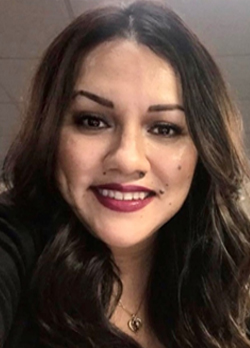 Woman with wavy, brown hair wearing a black crdigan over a purple blouse