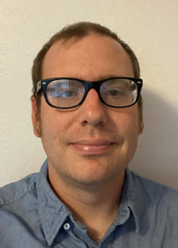 Man with short brown hair wearing black rimmed glasses and a blue button up shirt