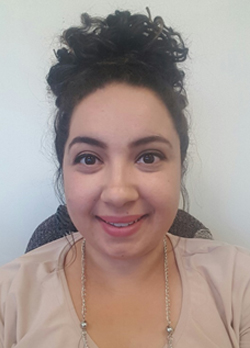 Woman with curly black hair pulled back in a bun wearing a tan shirt and silver necklace