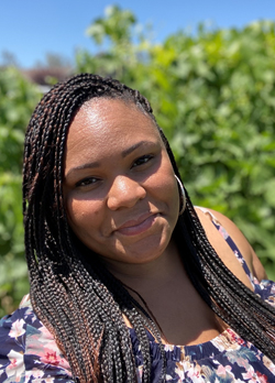 Woman with long, black, brown, braided hair wearing silver hoop earrings and a blue floral blouse