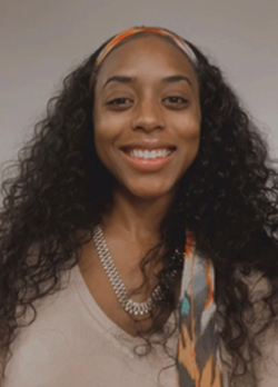 woman with dark brown curly hair wearing a tan sweater