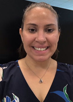 Woman with hair pulled back wearing a navy floral blouse with silver necklace