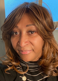 woman with wavy brown hair wearing a black turtleneck with white stripes and a black jacket